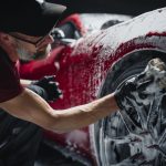Red Sportscar's Wheels Covered in Shampoo Being Rubbed by a Soft Sponge at a Stylish Dealership Car Wash. Performance Vehicle Being Washed in a Detailing Studio